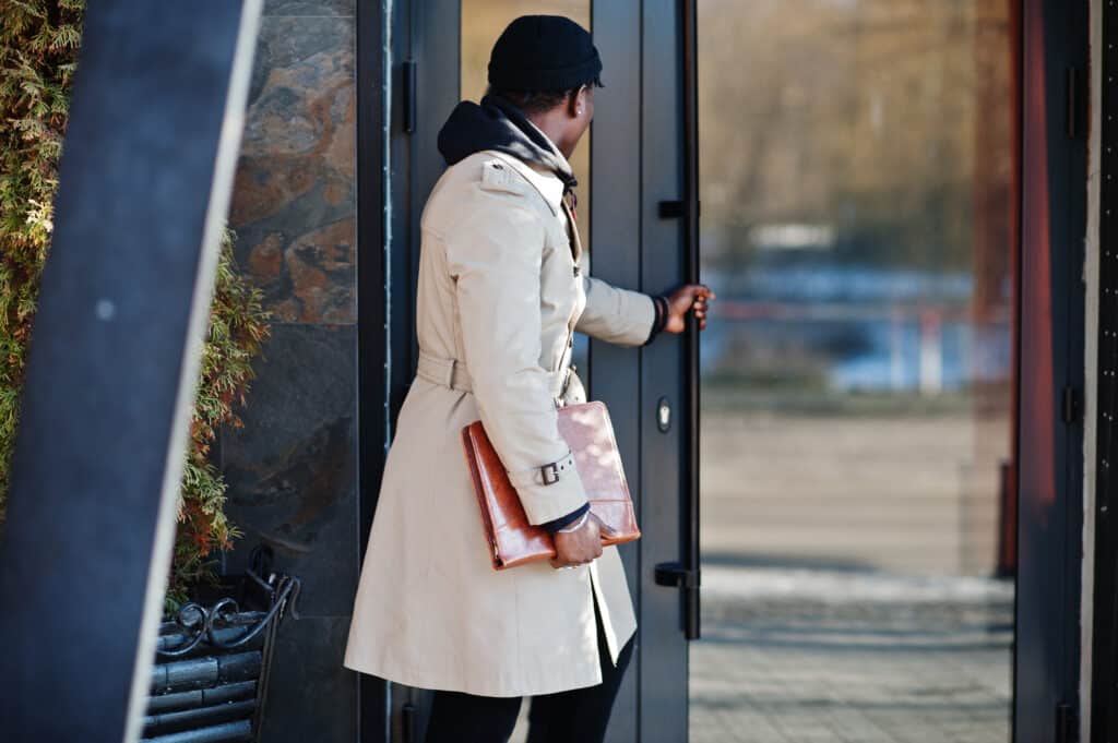 Handsome african american man posing outside in black hat and beige coat with folder in hand.